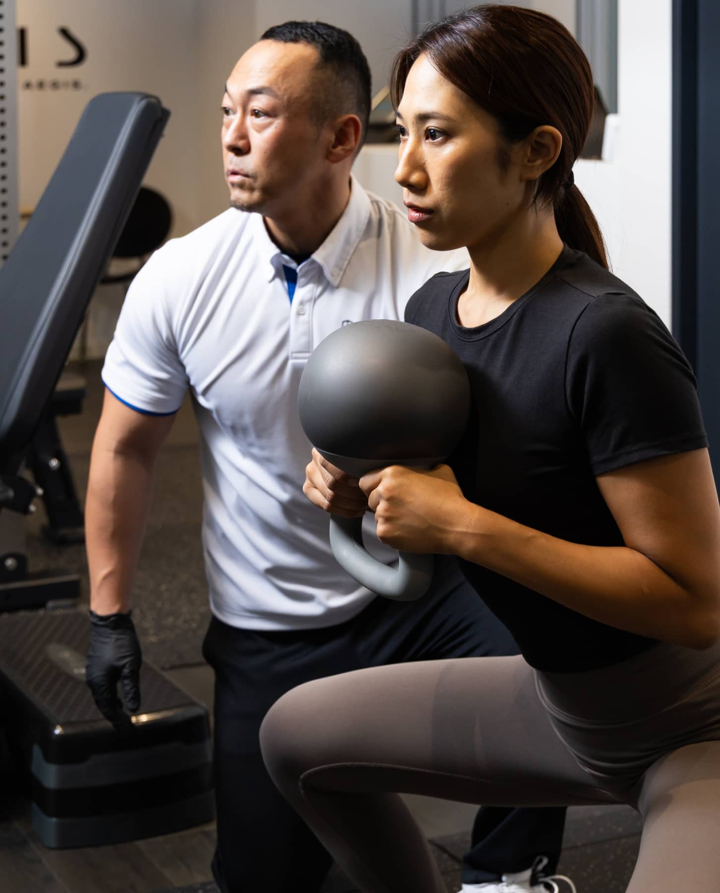 トレーナーの指導を受けながらダンベルでトレーニングする女性